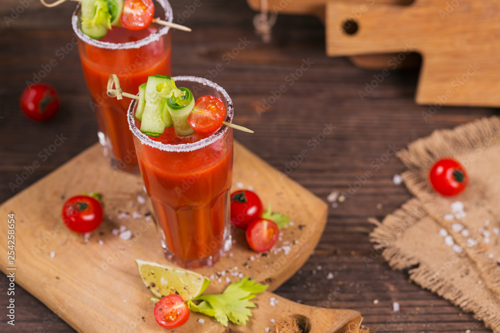 Two glasses of tomato juice decorated with fresh tomatoes, cucumber and leaves on a wooden background Two glasses of tomato juice decorated with fresh tomatoes, cucumber and leaves on a wooden background