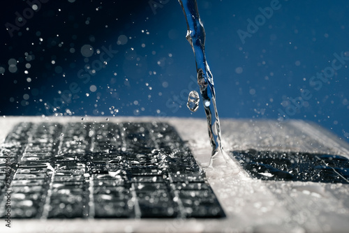 A stream of water pours on the laptop keyboard. photo