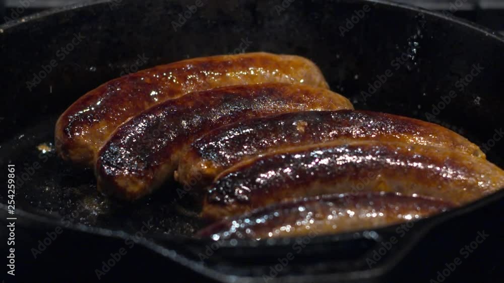 Huge, tasty sausages popping with juice and flavor are being fried on a black iron pan. Huge, tasty sausages popping with juice and flavor are being fried on a black iron pan.