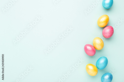Border made of colorful Easter eggs on turquoise background. Top view, copy spase, minimal styled.