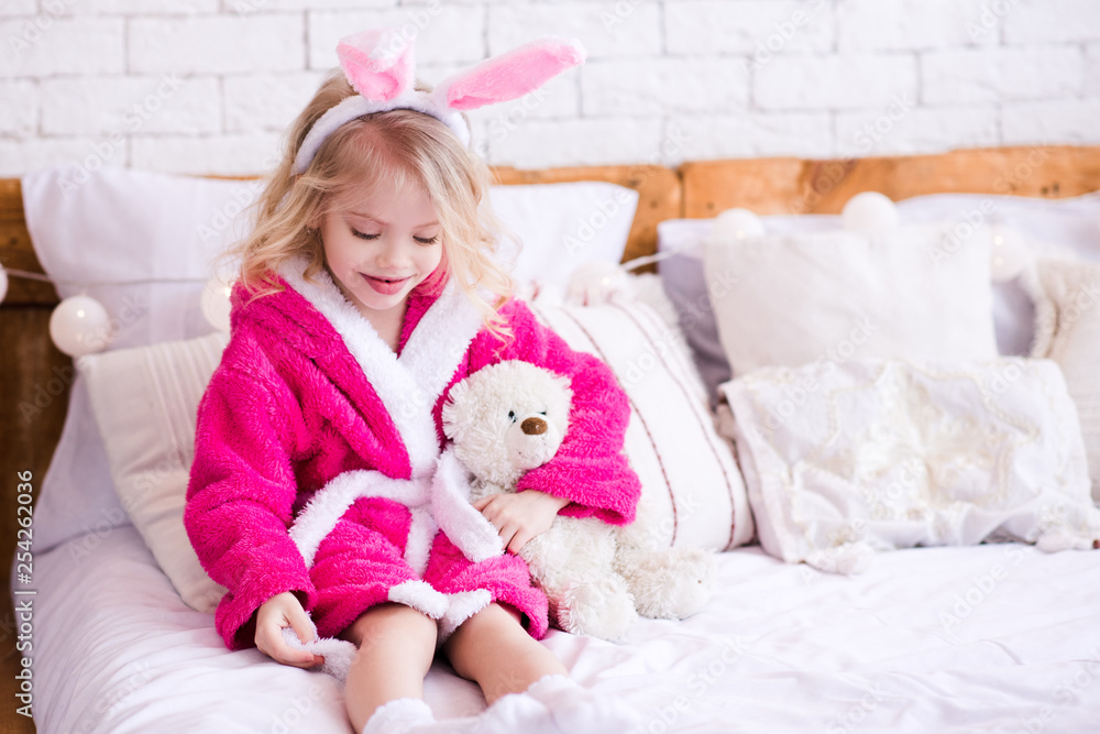 Hapy kid girl 3-4 year old playing with teddy bear wearing bathrobe sitting in room. Good morning. Hapy kid girl 3-4 year old playing with teddy bear wearing bathrobe sitting in room. Good morning.