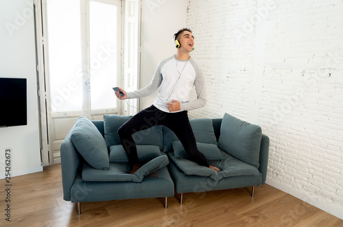 Young man in his twenties with headphones listening to music and dancing on sofa at home photo