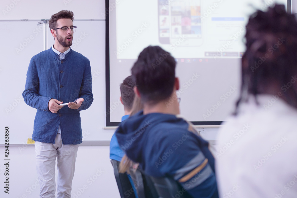 Group of students study with professor in modern school classroom. Male professor explain to students and interact with them, helping a students during class. Group of students study with professor in modern school classroom. Male professor explain to students and interact with them, helping a students during class.