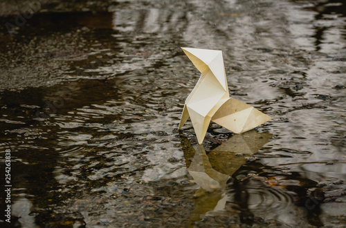 Origami paper figure on the background of a gloomy city street and puddles