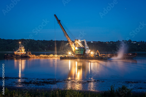 A huge crane with a metal bucket on the ship produces sand on the volga river on a night. concept of the resource industry. landscape.