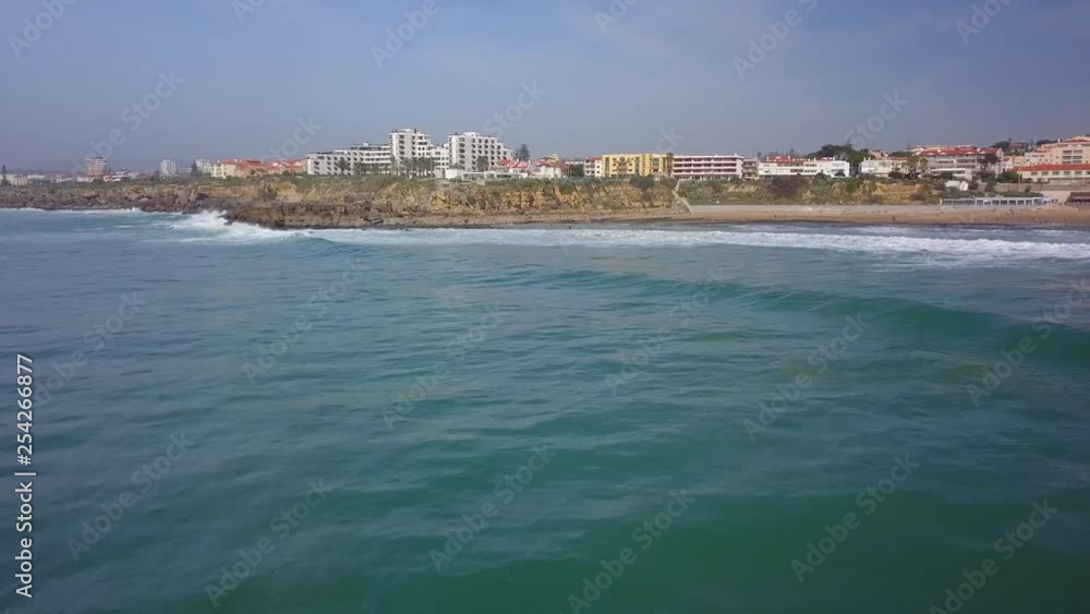 Aerial, drone shot, towards waves hitting the coast of Praia de Sao pedro do Estoril, on a sunny day, in Cascais, Portugal Aerial, drone shot, towards waves hitting the coast of Praia de Sao pedro do Estoril, on a sunny day, in Cascais, Portugal