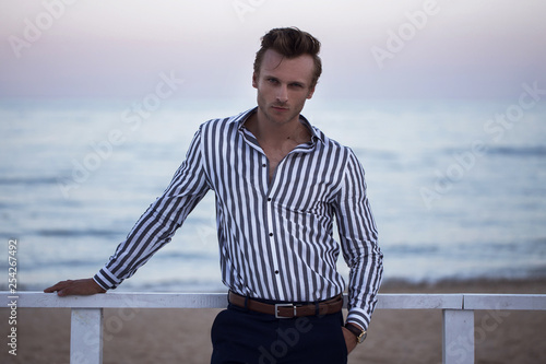 young attractive guy on the ocean meets sunset. The concept of fashion style on vacation