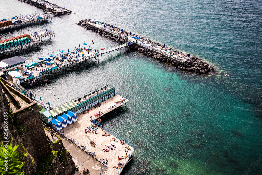Sorrento coastline with bathing platforms built out over the sea and harbour in distance, Sorrento, Italy