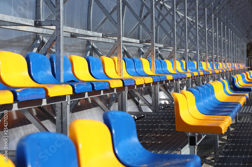 New stands on the football field of metal light construction with plastic seats in blue and yellow. Places for fans in the stadium. Going to the audience for sports competitions. Shelter from the run