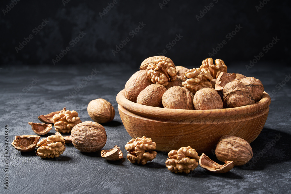 Raw walnut in wooden bowl on black background, close-up. Raw walnut in wooden bowl on black background, close-up.