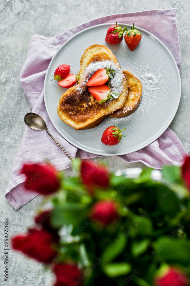 Breakfast with French toast and strawberries, vase with roses. Gray background, top view, space for text
