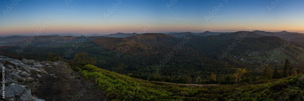 Big panorama of landscape mountain before sunrise. Mild foggy haze under the peaks. Clearly green bilberry shrub and gray rocks in the foreground.