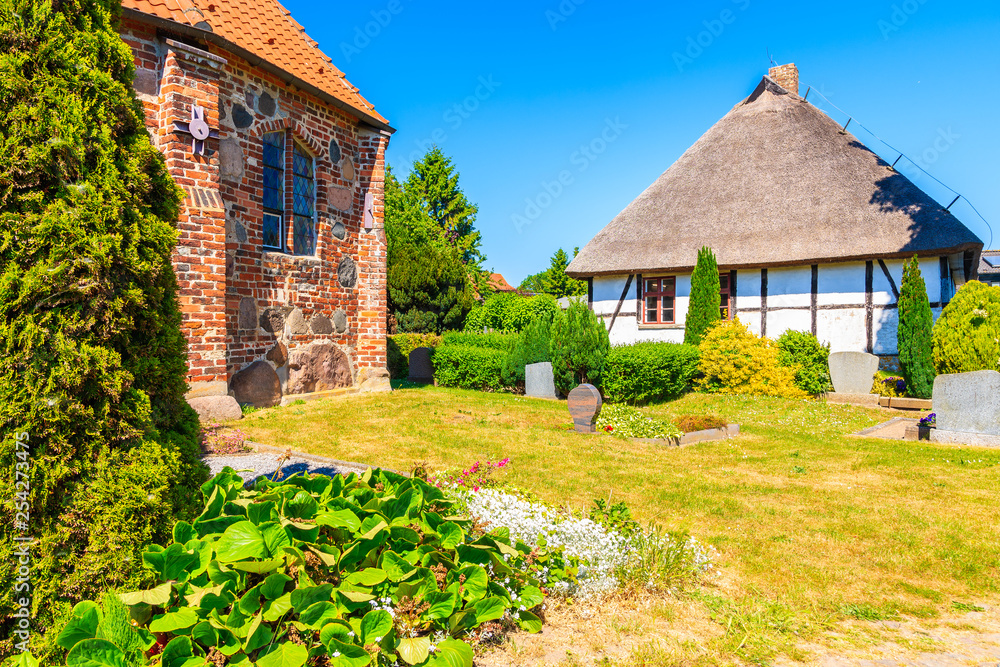 Traditional house with straw roof and old gothic church built from red bricks in Middelhagen village, Ruegen island, Baltic Sea, Germany