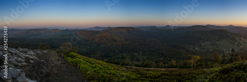 Big panorama of landscape mountain before sunrise. Mild foggy haze under the peaks. Clearly green bilberry shrub and gray rocks in the foreground.