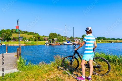 Young woman cyclist looking at Moritzdorf village in countryside spring landscape of Rugen island, Baltic Sea, Germany
