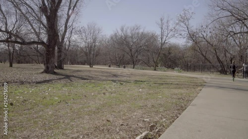 This is a wide shot of a jogger and a cyclist exercising in a park. The jogger and cyclist pass the camera while a Dog and his Owner are seen in the background. photo