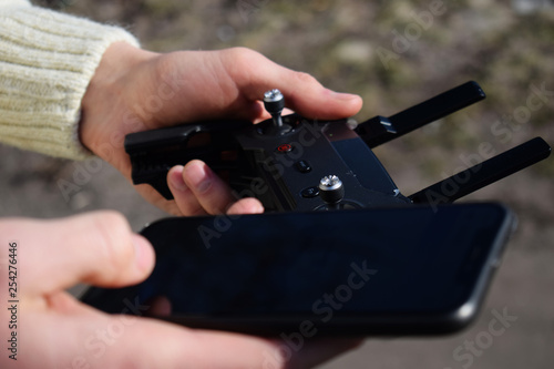 Remote control and smartphone in male hands. A man holding a transmitter and piloting some vehicles. A drone, radio controlled car or helicopter is running.