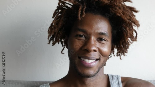 Happy man shakes up his dreads / afro as he smiles.