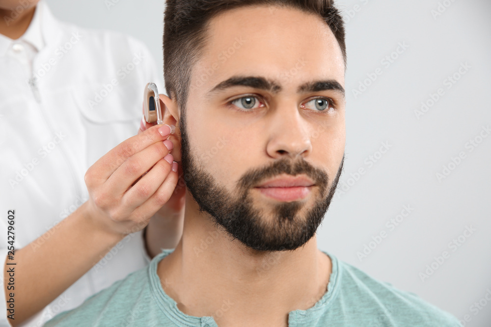 Obraz premium Otolaryngologist putting hearing aid in man's ear on white background