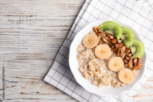 Bowl of quinoa porridge with walnuts, kiwi, banana and milk on wooden background, top view. Space for text