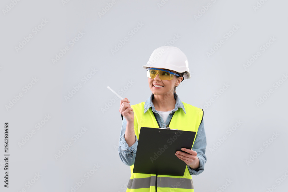 Female industrial engineer in uniform with clipboard on light background. Safety equipment Female industrial engineer in uniform with clipboard on light background. Safety equipment