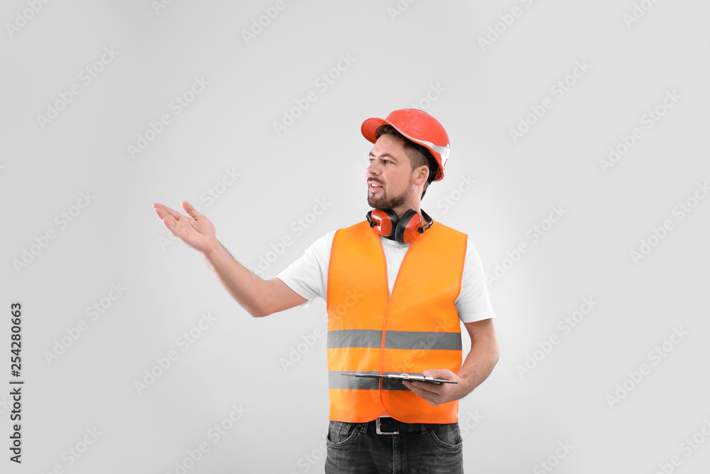 Male industrial engineer in uniform with clipboard on light background. Safety equipment