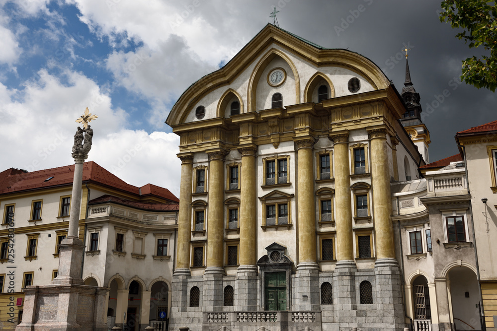 Spot of sun on the Ursuline Church of the Holy Trinity with marble statues of the Holy Trinity column in Ljubljana Slovenia with dark clouds