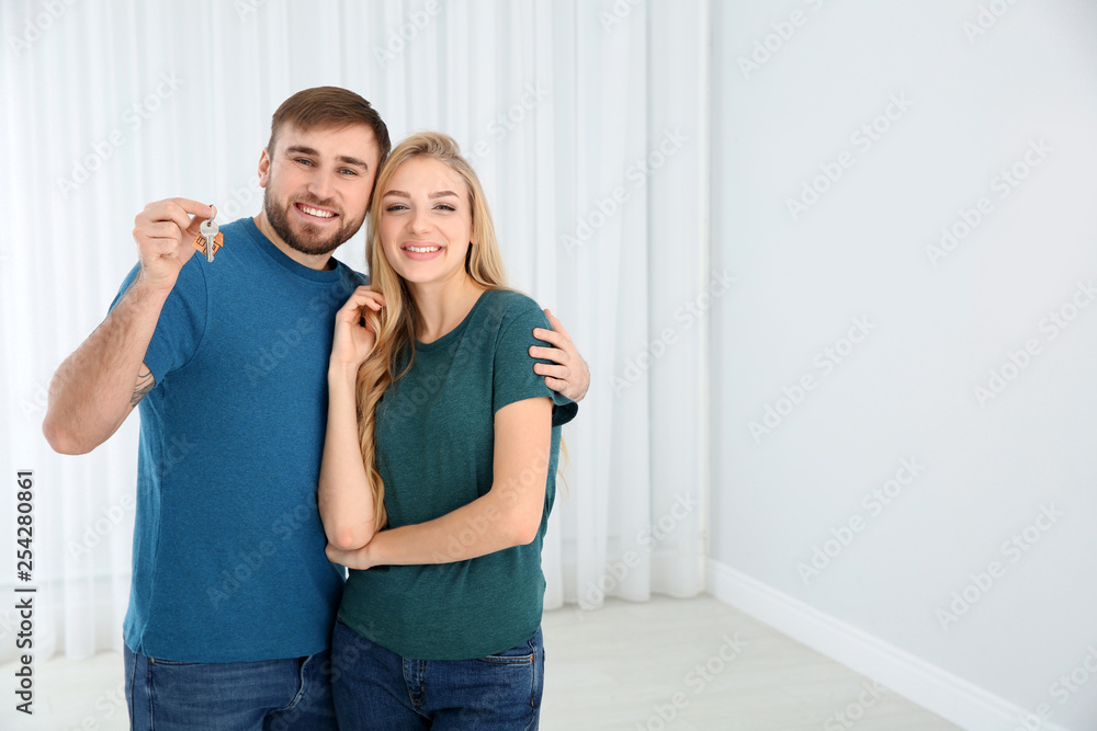 Happy young couple with key from their new house indoors, space for text Happy young couple with key from their new house indoors, space for text