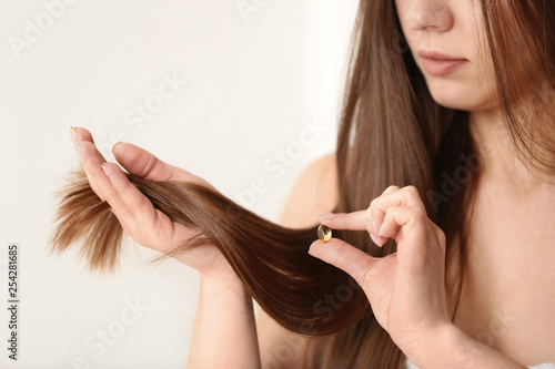 Woman holding vitamin capsule for hair health on light background, closeup