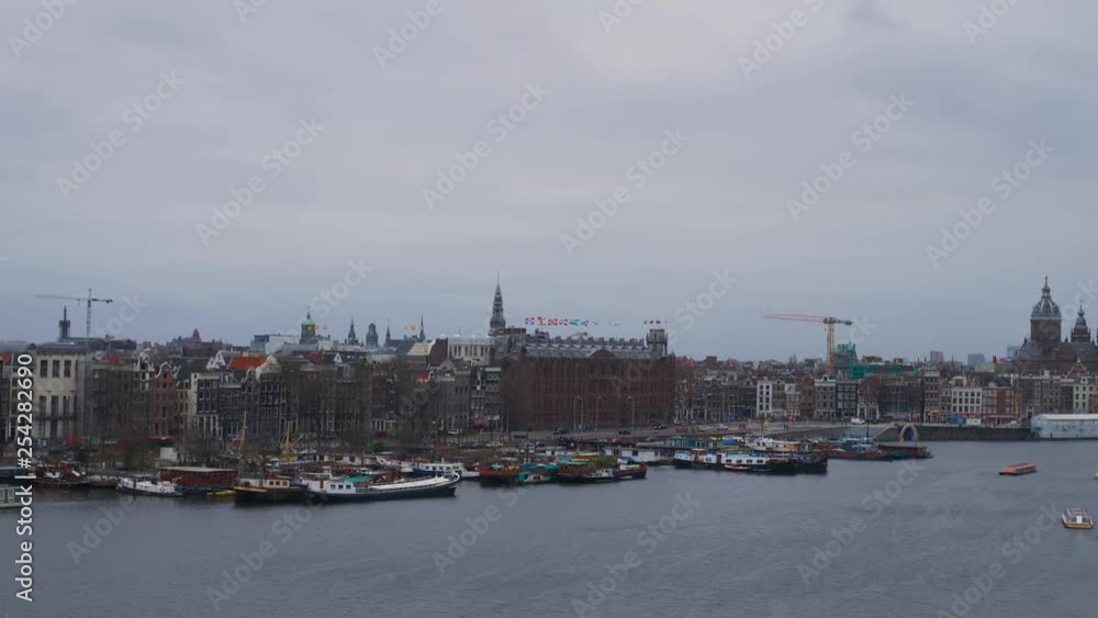 Observation of city exterior with boats in port. Pan right cityscape with embankment and sailing boats in water of channel under cloudy sky Observation of city exterior with boats in port. Pan right cityscape with embankment and sailing boats in water of channel under cloudy sky
