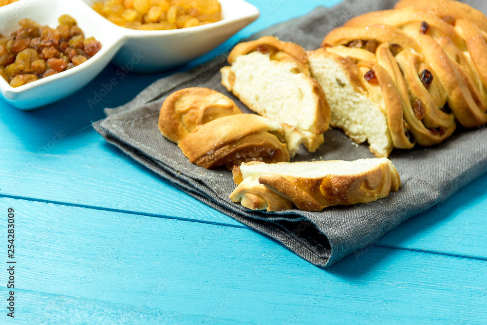 Piece of Sweet Braided Bread with raisins on kitchen towel on blue wooden background. Piece of Sweet Braided Bread with raisins on kitchen towel on blue wooden background.