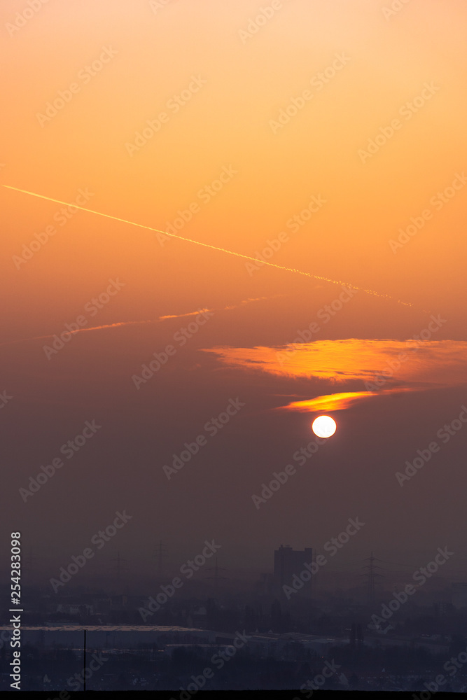Obraz premium Power lines in city on dawn. Silhouettes of urban buildings among smog on sunrise. Cables of high voltage on warm orange yellow sky