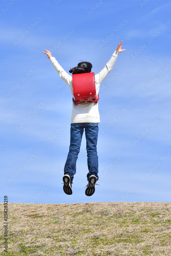 青空でジャンプする小学生の女の子 後姿 Stock Photo Adobe Stock