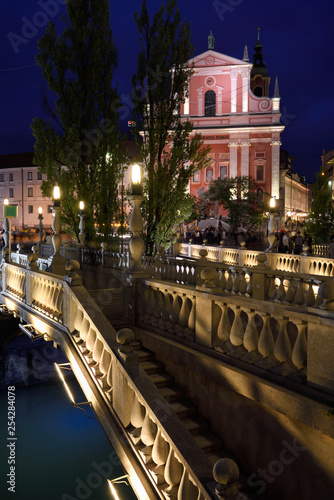 Lights on pink facade of Franciscan Church of the Annunciation and  ballustrades of Triple Bridge over Ljubljanica river Ljubljana Slovenia