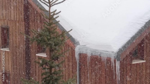 Strong snowfall in a mountain resort over wooden buildings with icicles and pine tree photo