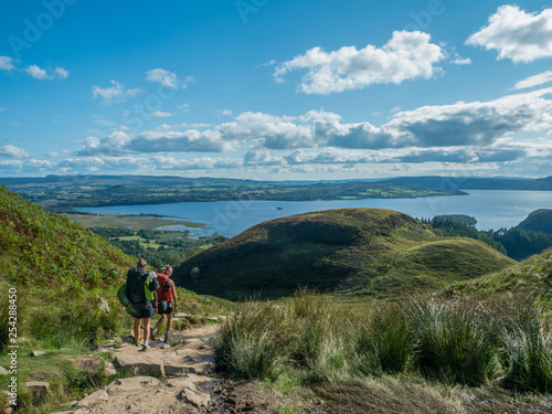 two girls hiking with beautiful lake (loch lomond) and green landscape on a sunny day