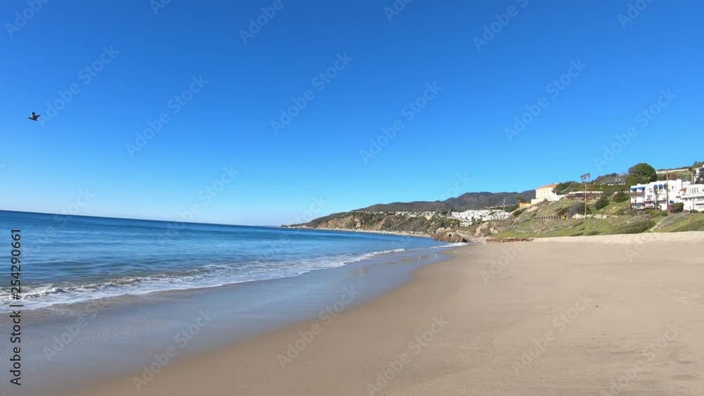 Waves breaking gently on Malibu beach, view of city on coastline and ocean Waves breaking gently on Malibu beach, view of city on coastline and ocean
