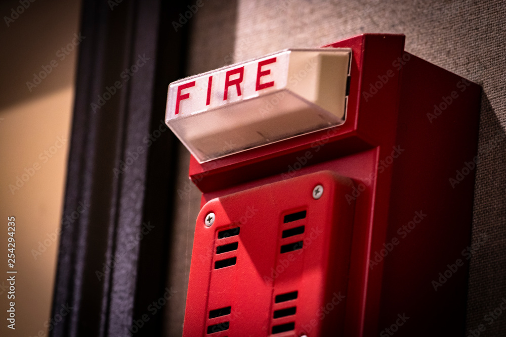 Red fire alarm/detector/siren/light system component on wall of school ...