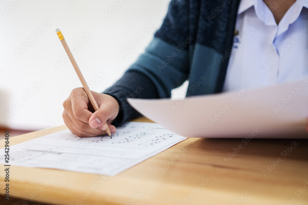 Students hands taking exams, writing examination room with holding pencil on optical form of standardized test with answers and english paper sheet on row desk chair doing final exam in classroom. Students hands taking exams, writing examination room with holding pencil on optical form of standardized test with answers and english paper sheet on row desk chair doing final exam in classroom.
