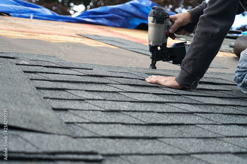Fotografie handyman using nail gun to install shingle to repair roof