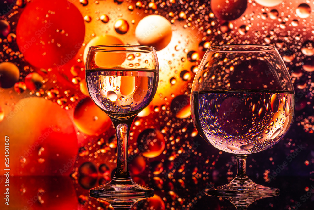 transparent glasses with water with oily drops on colorful background 