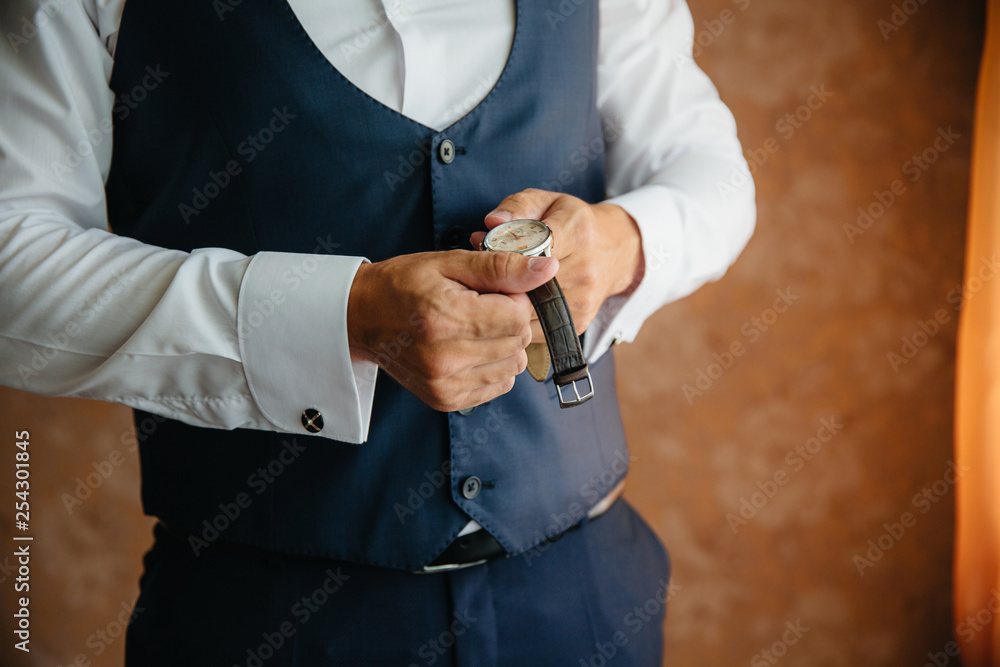 Close-up man puts on a gold watch with a leather belt, businessman is dressed in a stylish suit, a white shirt.