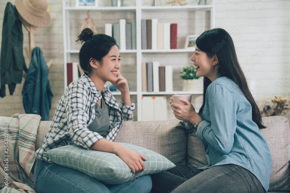 Two asian casual women relaxing on sofa with hot drink in new home. young girls chatting talking about funny things gossip laughing on couch in apartment. female roommates stay in dormitory together. Two asian casual women relaxing on sofa with hot drink in new home. young girls chatting talking about funny things gossip laughing on couch in apartment. female roommates stay in dormitory together.