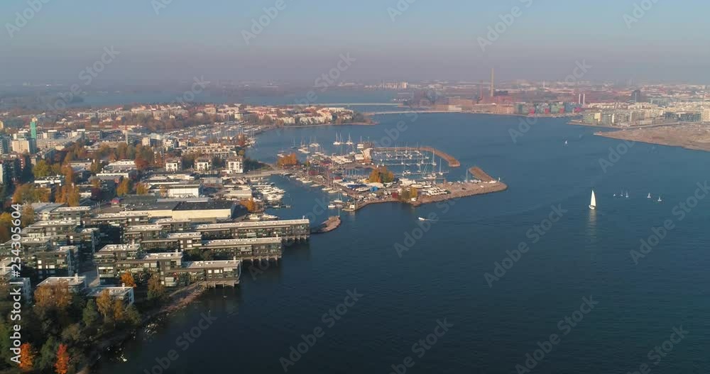 Aerial, reverse, drone shot, above the sea, of buildings and boats, at Lauttasaari harbor, on a sunny, fall day, in Helsinki city, Finland Aerial, reverse, drone shot, above the sea, of buildings and boats, at Lauttasaari harbor, on a sunny, fall day, in Helsinki city, Finland