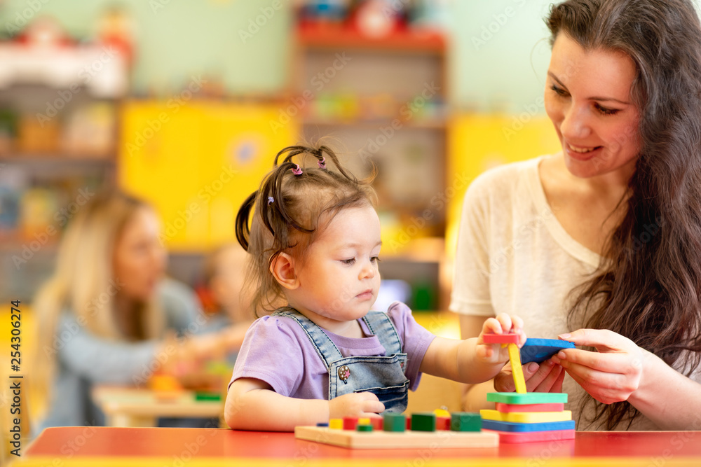 Babies with teachers playing with developmental toys in nursery Babies with teachers playing with developmental toys in nursery