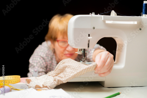 woman in glasses using sewing machine or threading on dark background b