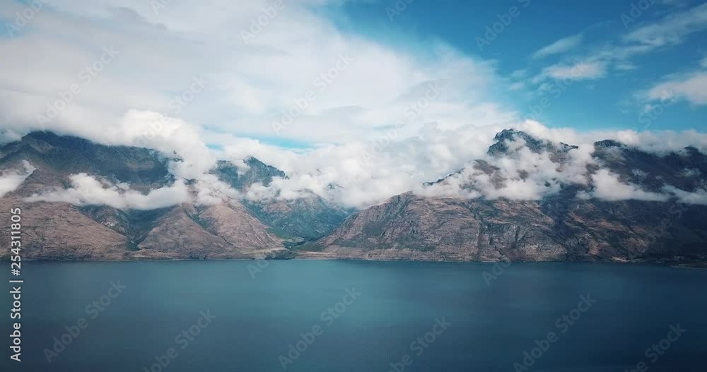 Drone shot of Lake Wakatipu, Queenstown, New Zealand, with the Remarkable mountains in the background, in a bright sunny day with clouds surrounding the mountains Drone shot of Lake Wakatipu, Queenstown, New Zealand, with the Remarkable mountains in the background, in a bright sunny day with clouds surrounding the mountains