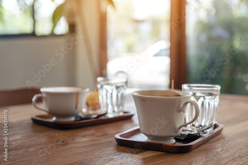 Closeup image of white mugs of hot coffee and glasses of water on wooden table in cafe