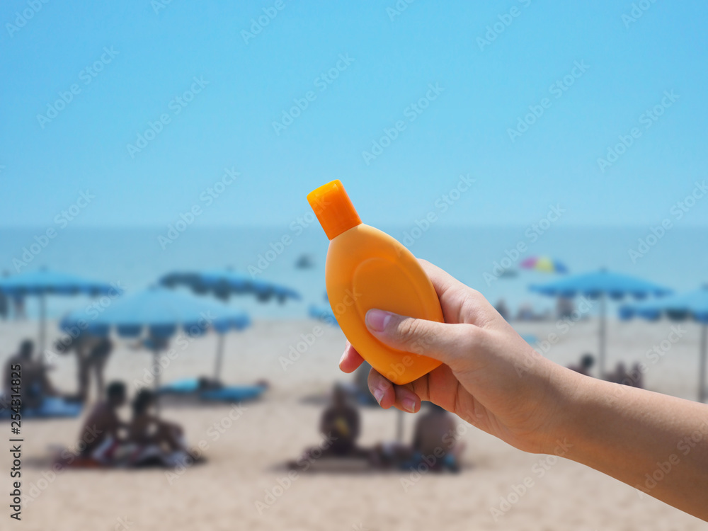 hand holding sunblock cream bottle over blurred summer beach background hand holding sunblock cream bottle over blurred summer beach background