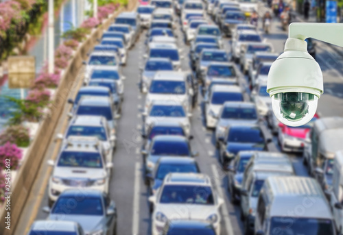 Closeup of CCTV security camera on abstract Blurred photo of traffic jam with rush hour on the road in the big city.